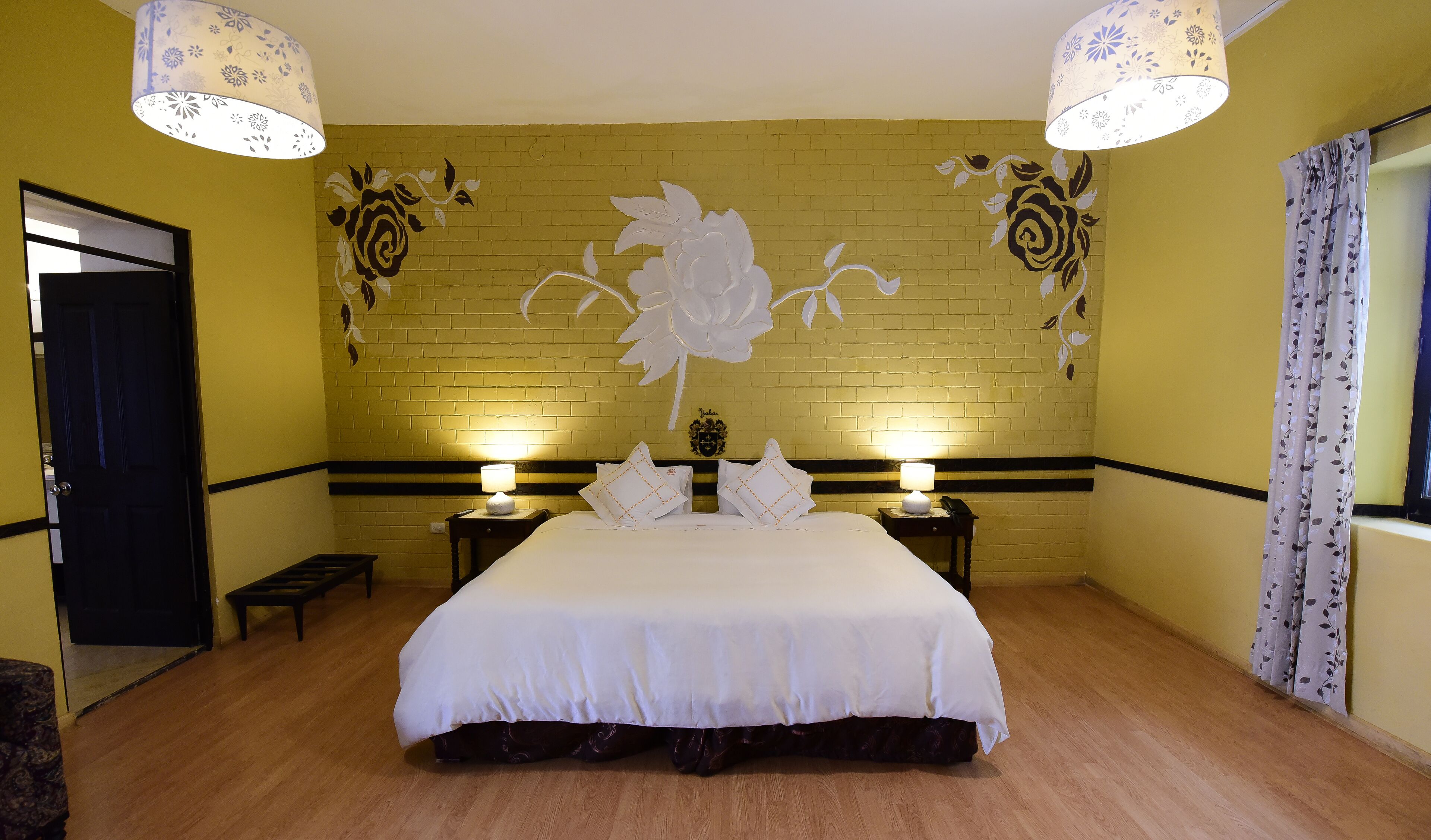 Una habitación de hotel con una cama grande, dos mesitas de noche con lámparas, un muro con diseño de ladrillo y un mural floral.