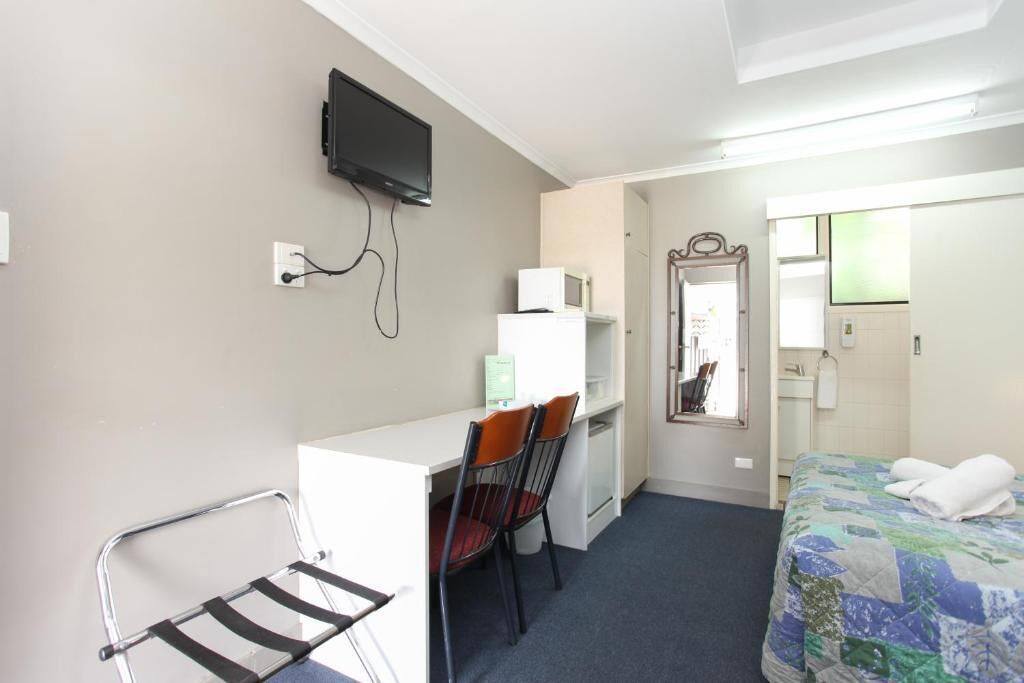 A hotel room with a desk, chairs, a bed, a television, and a mirror.