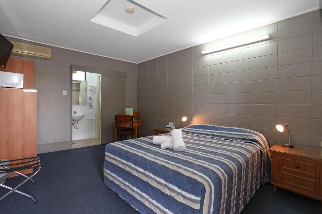 Une chambre d’hôtel comprenant un lit, une table de chevet et un bureau avec une chaise.