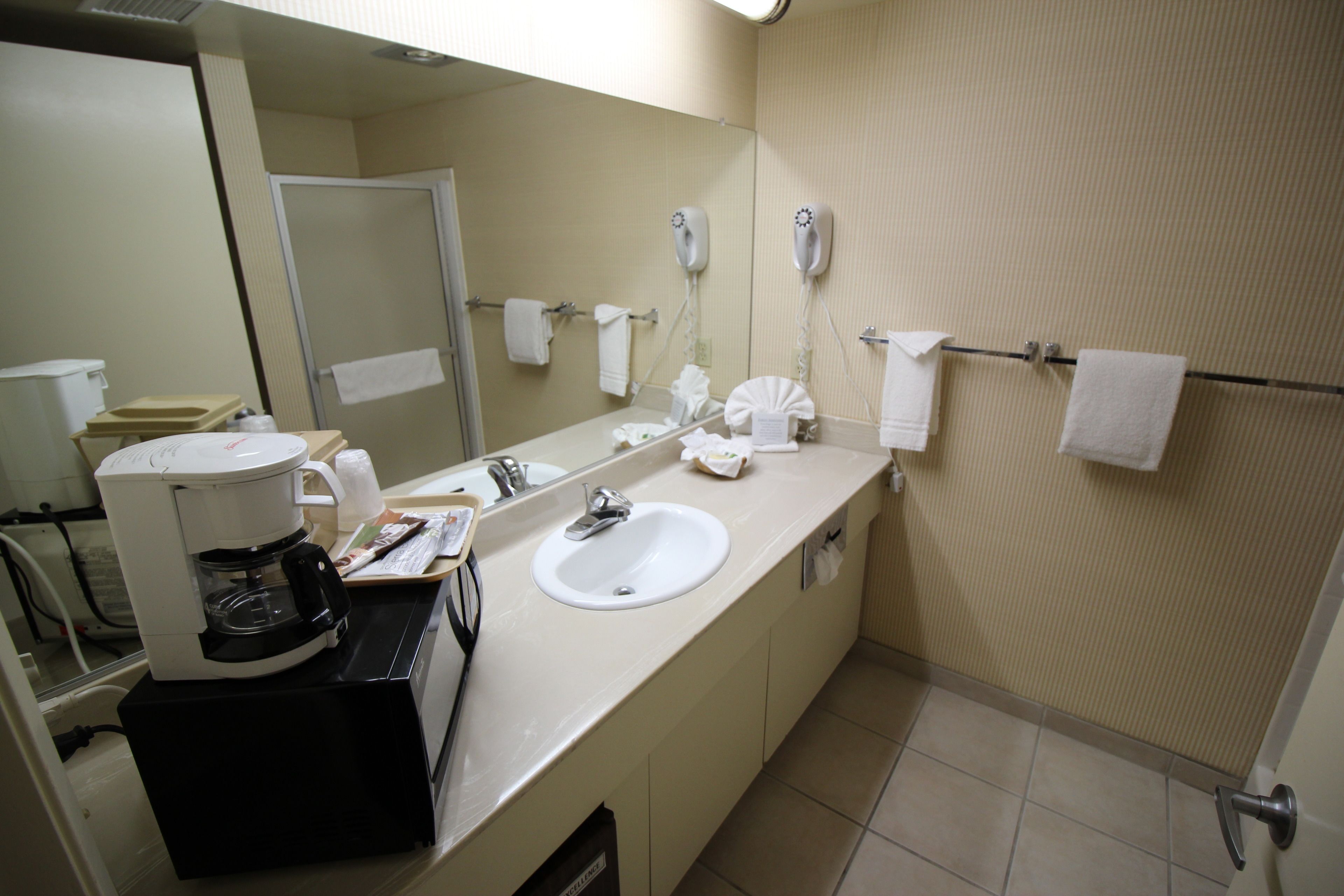 Casa de banho de hotel com pia, espelho, porta-toalhas e máquina de café.