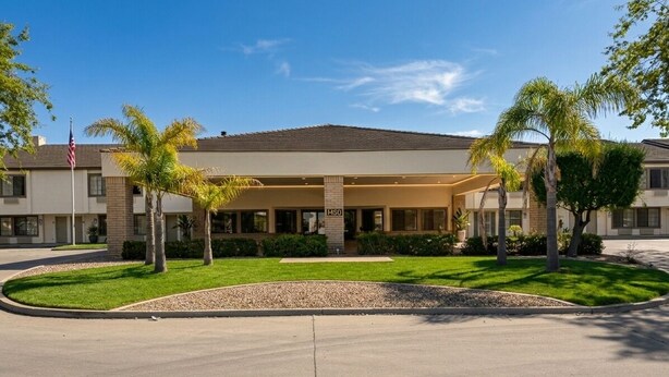 A hotel with a covered entrance, palm trees, and a clear sky. - Inn of Lompoc (Lompoc)