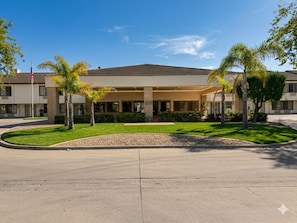 A hotel with a covered entrance, palm trees, and a clear sky.