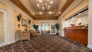 A spacious lobby with a patterned carpet, wooden paneling, a chandelier, and a reception desk. - Inn of Lompoc (Lompoc)