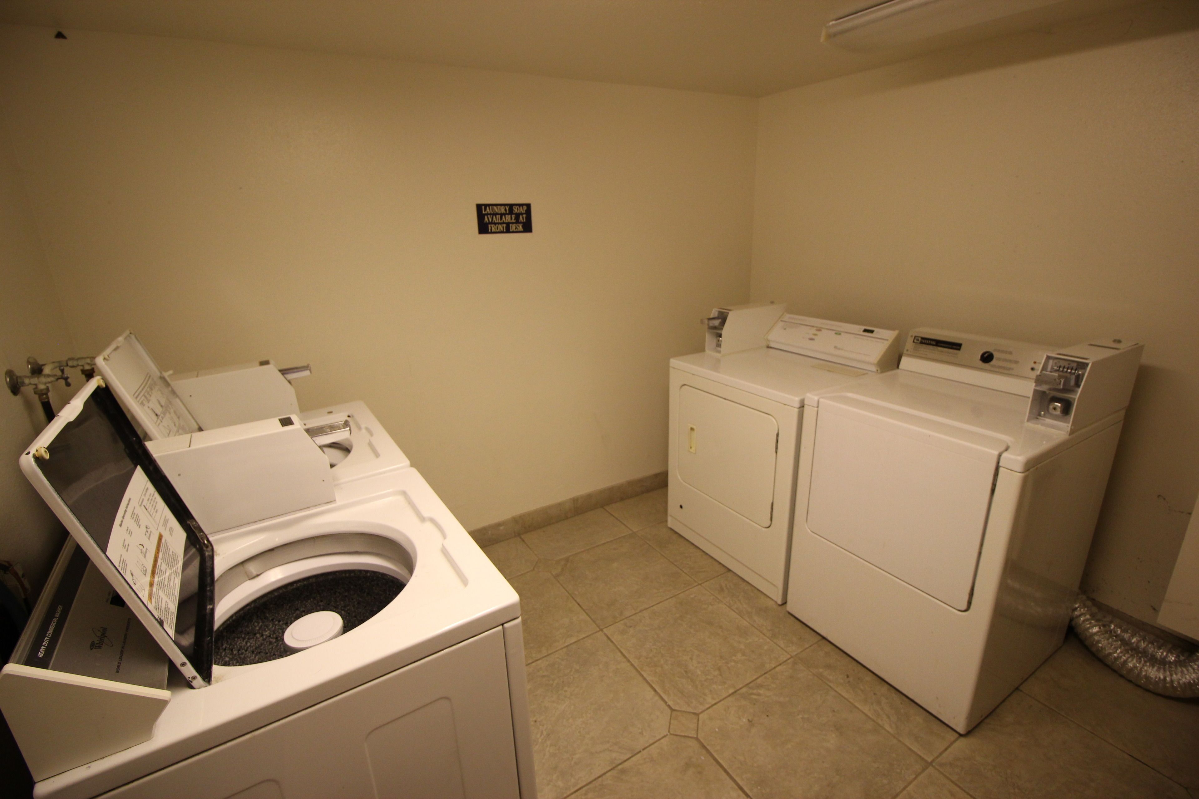 A laundry room with a front-loading washer and dryer, a wall-mounted sign, and a vent on the right.