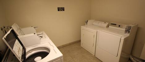 A laundry room with a front-loading washer and dryer, a wall-mounted sign, and a vent on the right.