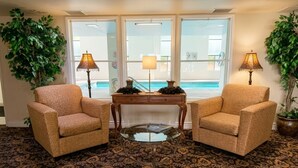 A room with two armchairs, a glass-top table, and two lamps. There is a large window with a view of a pool. - Inn of Lompoc (Lompoc)