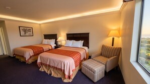 A hotel room with two beds, a chair, a lamp, and a window with a view. - Inn of Lompoc (Lompoc)