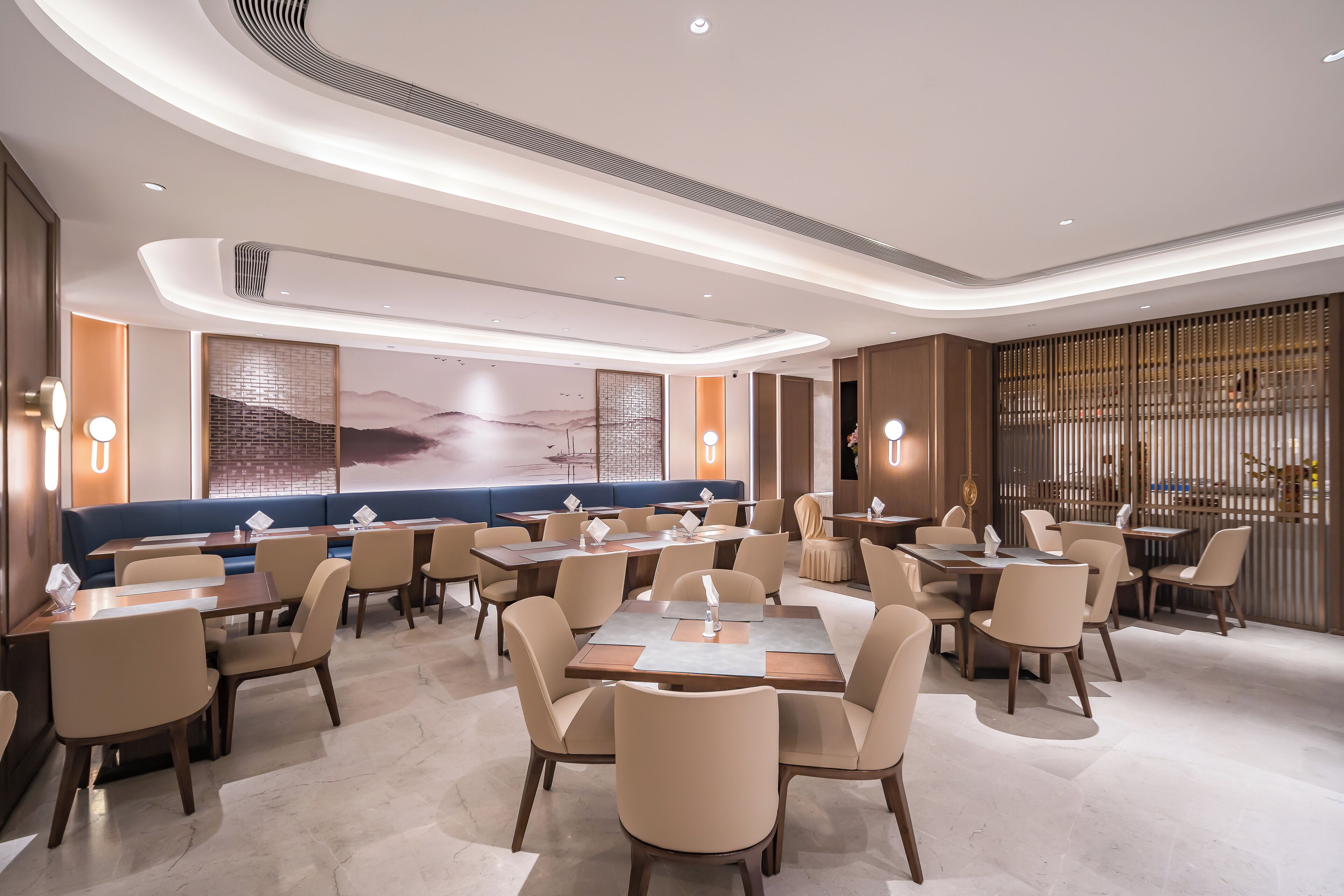 A modern restaurant with round tables and booths, ambient lighting, and a large mural on the wall.