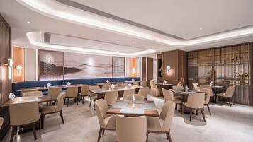 A modern restaurant with round tables and booths, ambient lighting, and a large mural on the wall.