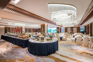 A banquet hall with round tables, a buffet, and a large chandelier.