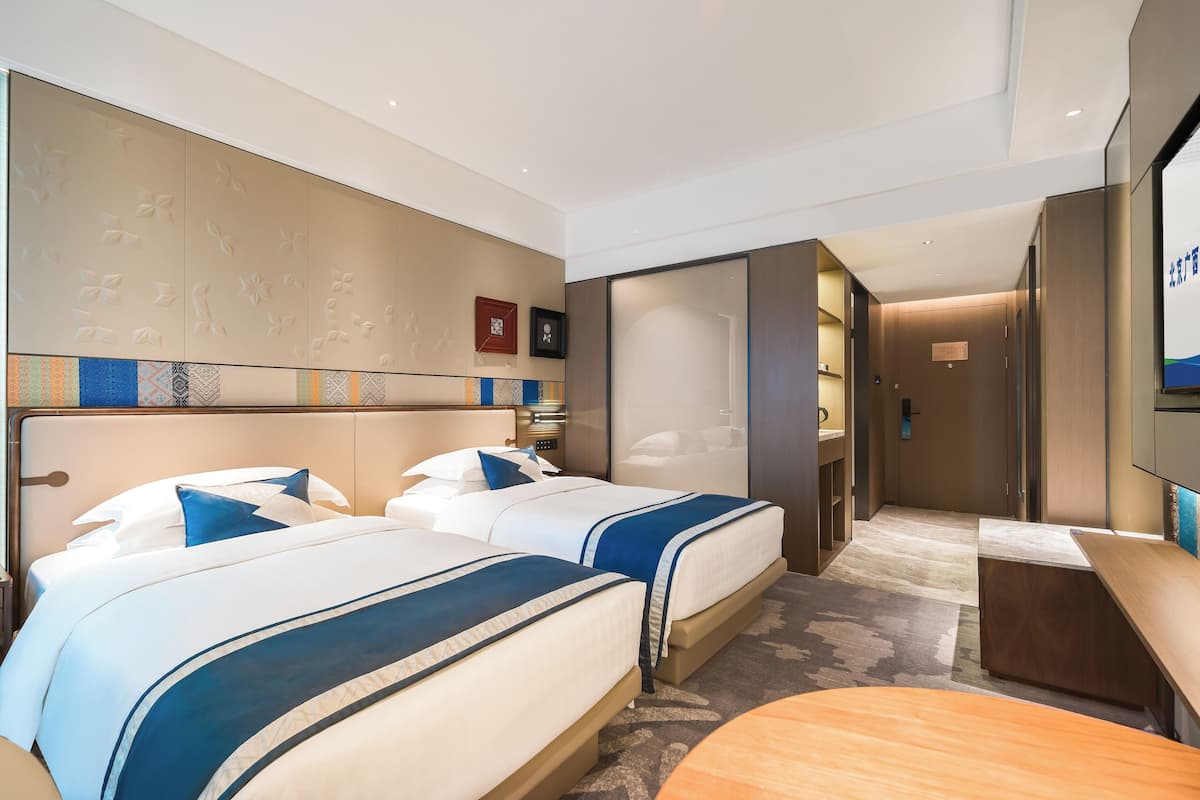 A hotel room with two beds, a desk, a mirror, and a wardrobe.