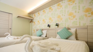 Habitación de hotel con dos camas, cada una con una colcha blanca y almohadas a juego. Hay toallas con forma de cisne decorativas sobre las camas. La habitación tiene una pared verde claro con estampado floral y un cabecero de madera.