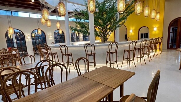 Un amplio comedor interior con mesas y sillas de madera, lámparas colgantes y ventanas grandes.