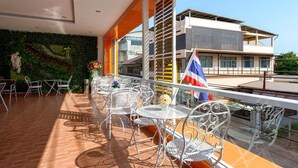 Un balcón con mobiliario exterior, una bandera y un edificio moderno al fondo.