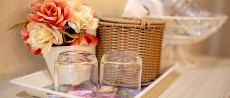 Un panier en osier contenant une composition florale et deux récipients en verre, le tout posé sur un plateau.