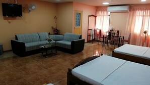A hotel room with a sofa, two single beds, a small table with a vase, a TV mounted on the wall, and a fan. - Sunshine Hotel & Hall (Trincomalee)