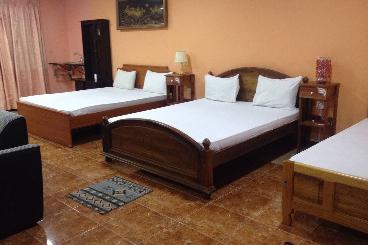 A hotel room with two wooden beds, a small desk, a chair, a nightstand, a lamp, and a painting on the wall.
