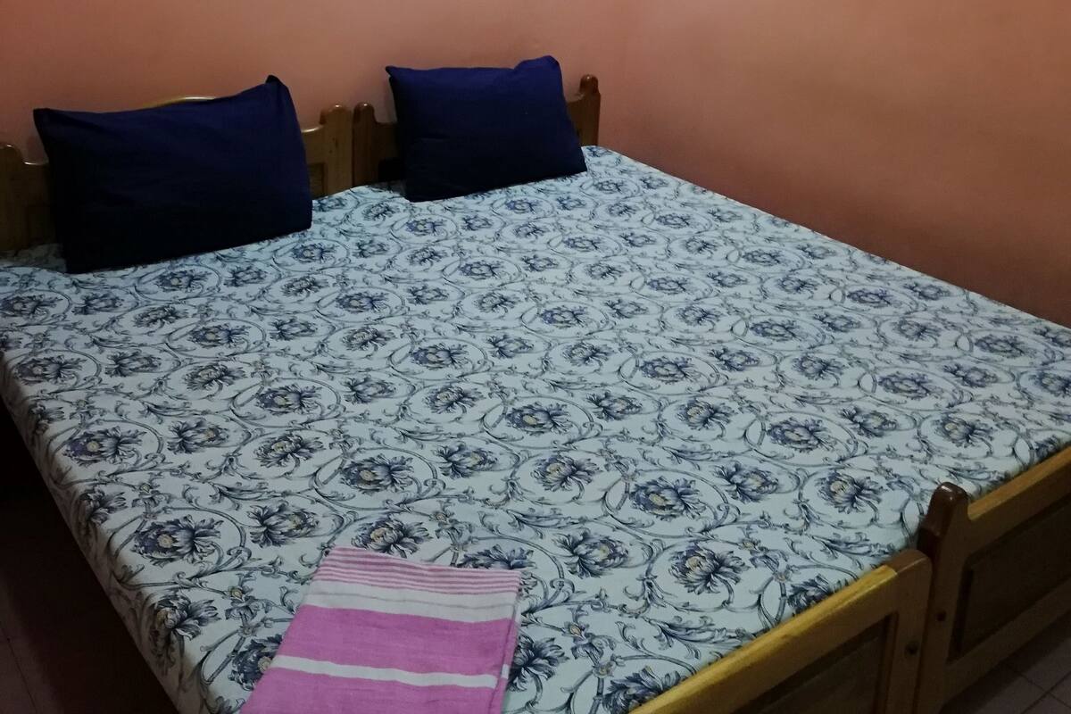 A single bed with a floral-patterned bedspread, two dark blue pillows, and a pink striped blanket.