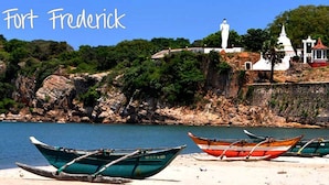 Boats on a sandy beach near a fort with a statue and a white building. - Sunshine Hotel & Hall (Trincomalee)