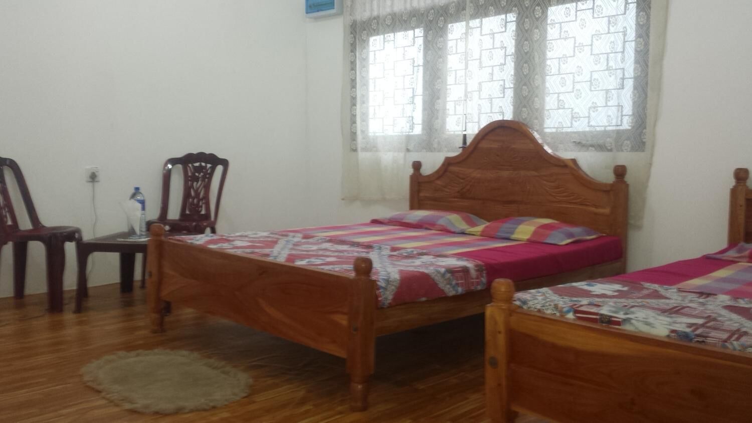 A bedroom with two wooden beds, a chair, a small table, and a window with patterned curtains.