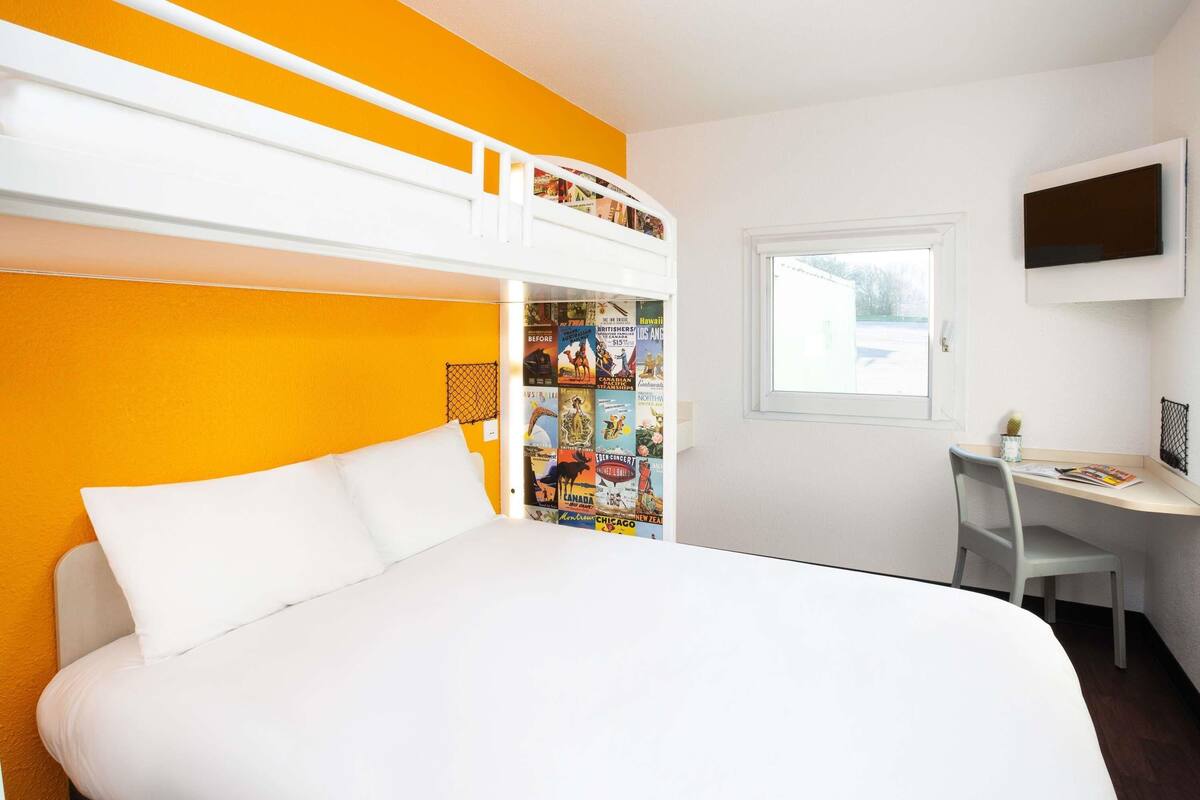A room with a bunk bed, a desk, a chair, a TV, and a window.