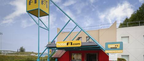 A hotel with a distinctive blue and yellow sign, a red entrance, and a parking area with a green bike lane.