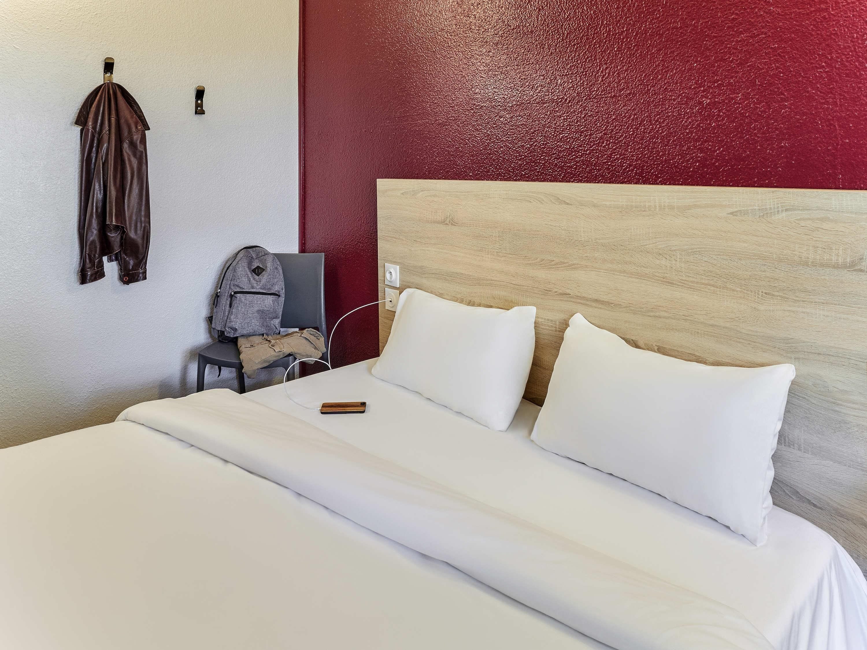 A neatly made bed with white bedding, a wooden headboard, and a red accent wall.