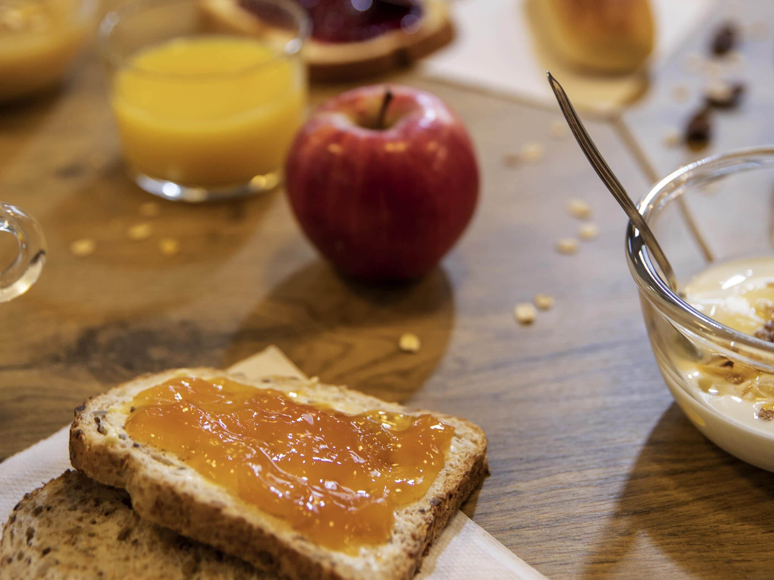 Aamiaispöytä, jossa on paahtoleipää, omena, appelsiinimehua ja muroja.