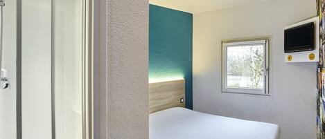 Una habitación de hotel con cama, ducha, ventana y televisión.