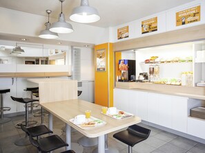 Um café moderno com mesa de madeira, cadeiras pretas e um balcão com diversos alimentos.