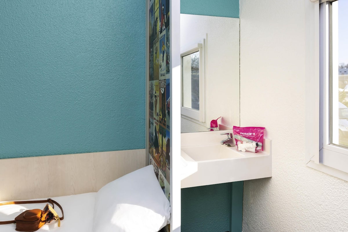 Une chambre d’hôtel avec un lit, une salle de bain comprenant un lavabo et un miroir, et une fenêtre donnant sur un paysage agréable.