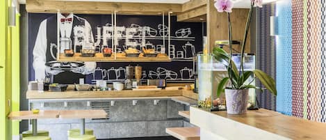 Una cafetería con mostrador, taburetes, una planta y un menú en una pizarra.