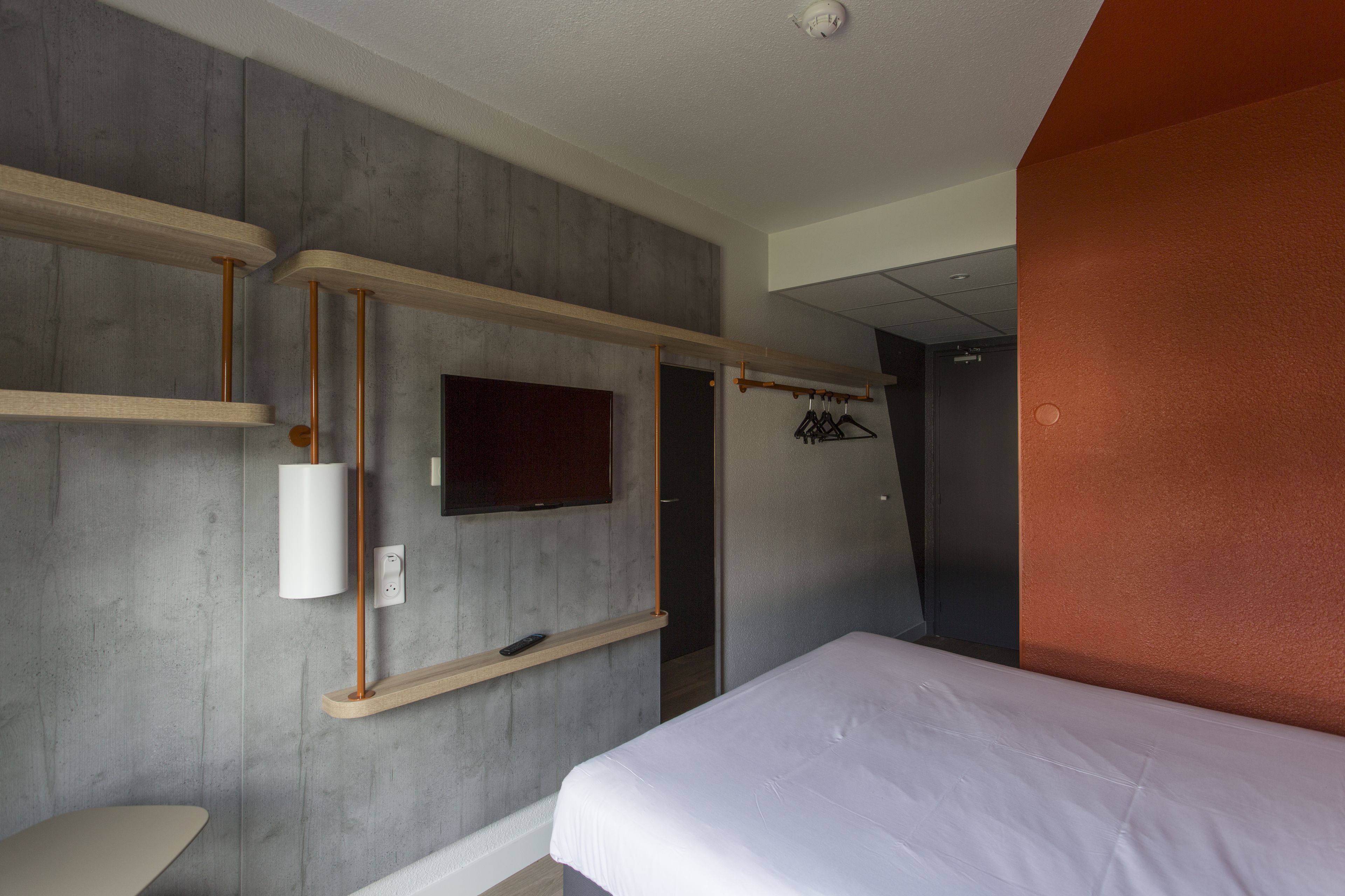 A bedroom with a bed, a mounted TV, and a coat rack.