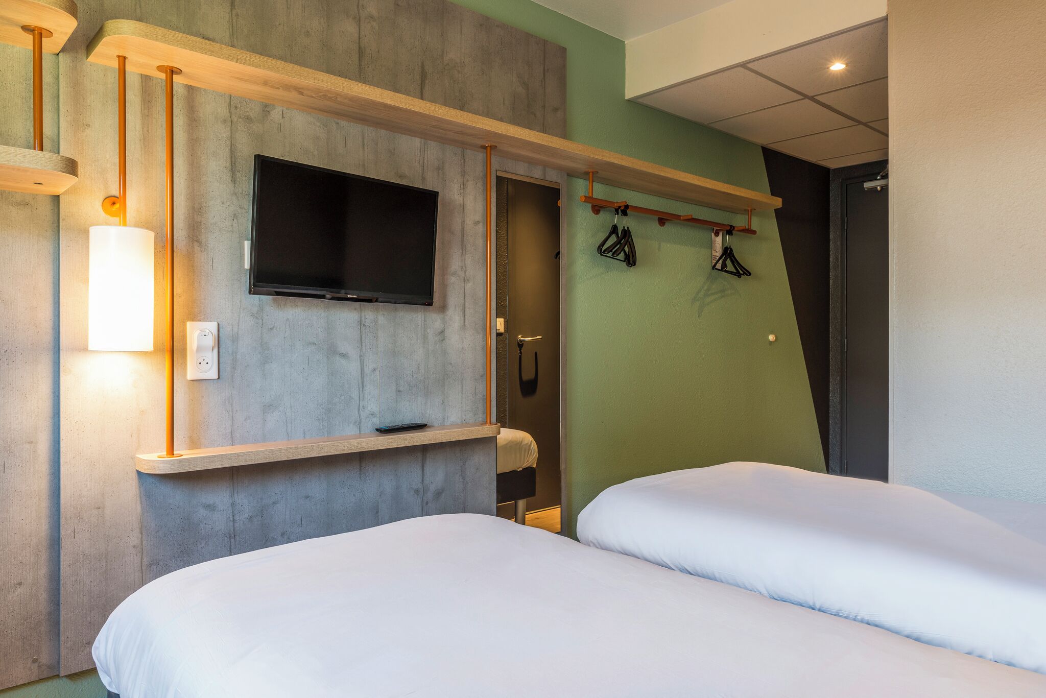 A hotel room with two beds, a mounted TV, a light fixture, and a coat rack.