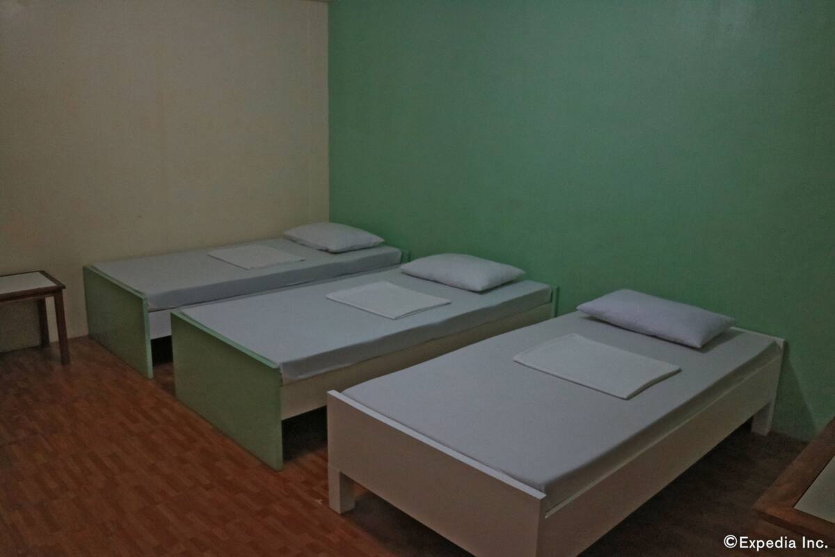 A room with three single beds aligned against a green wall, wooden flooring, and a small table to the left.