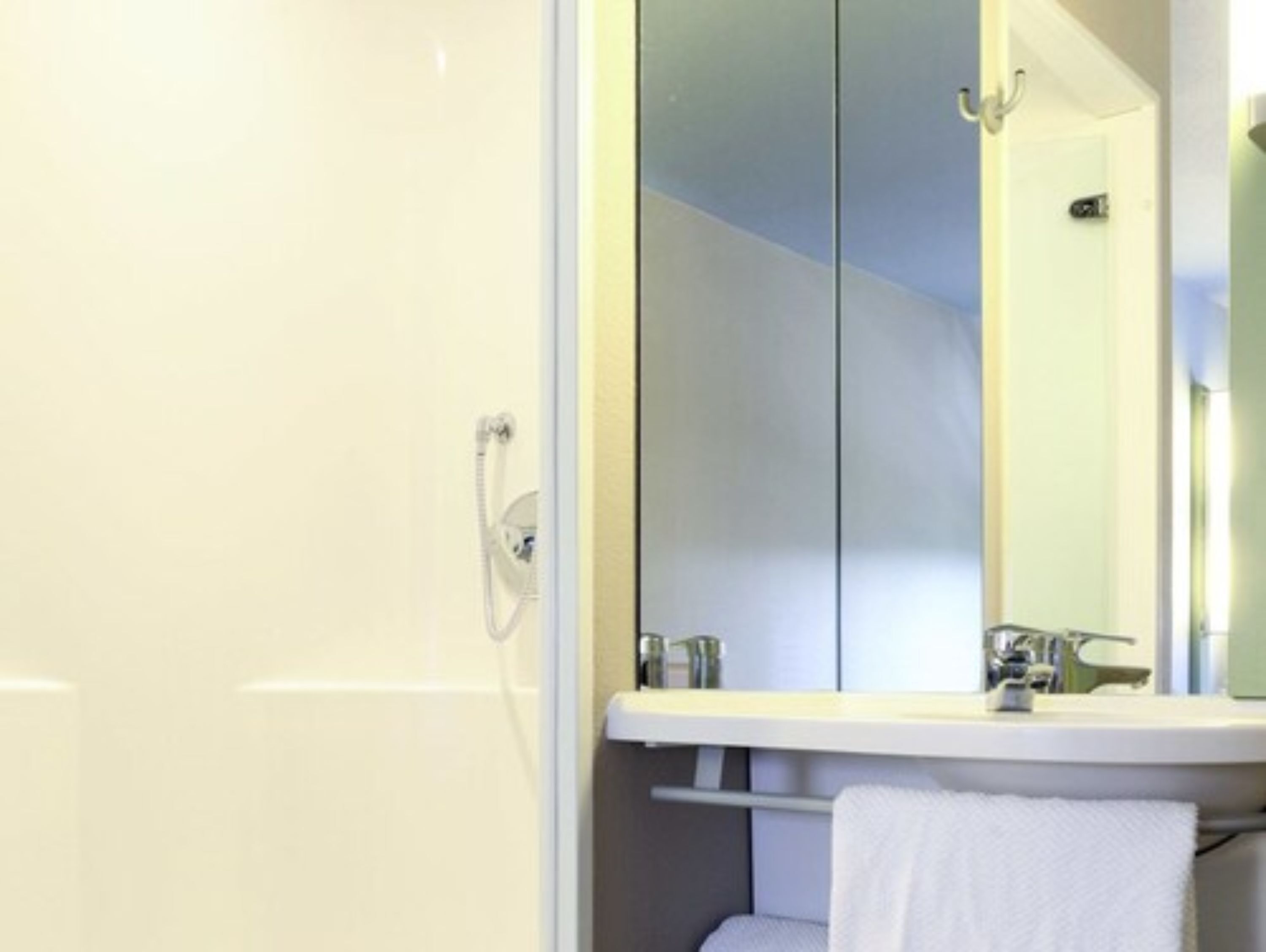 Un baño con lavamanos blanco, espejo y toallero.