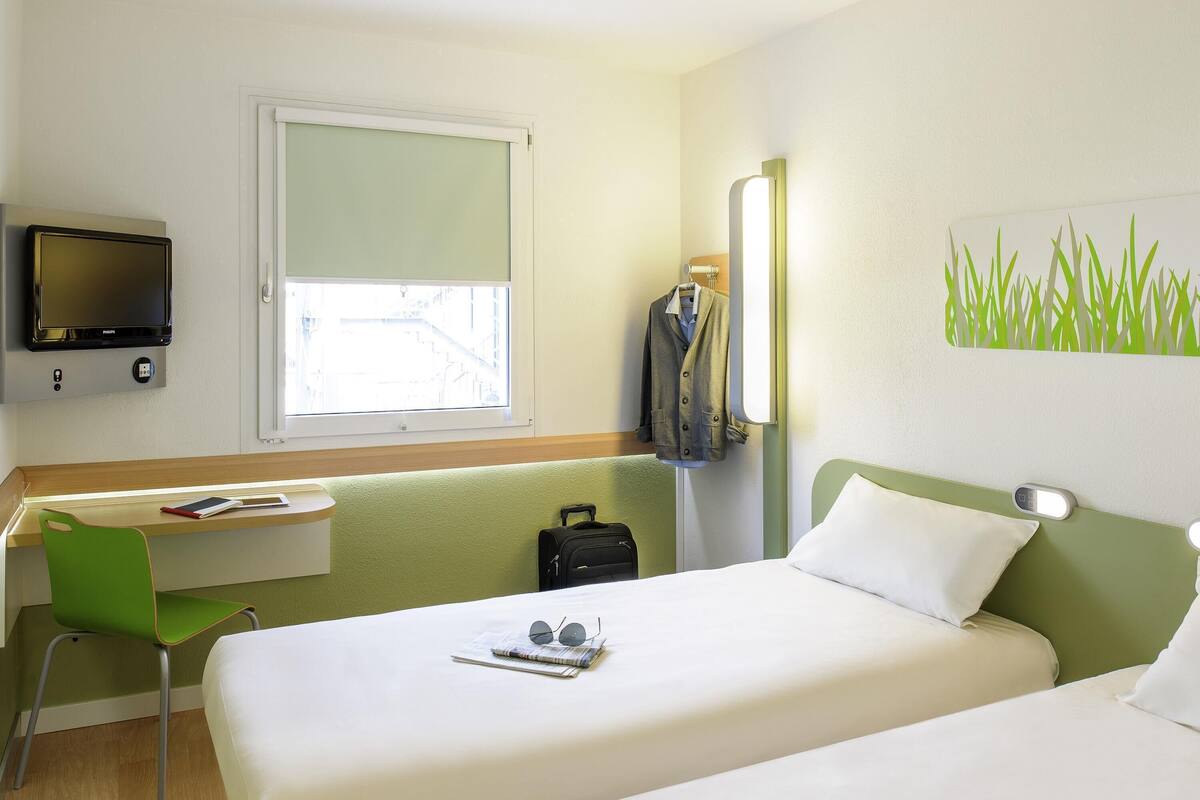 A hotel room with a bed, a desk, a chair, a TV, and a window.