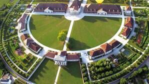 Vista aérea de un gran complejo de edificios circulares, con un césped central, rodeado de estructuras más pequeñas y jardines cuidados.