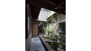 Ein traditioneller japanischer Garten mit einem Kiesweg, einem hölzernen Tor und einem kleinen Baum.