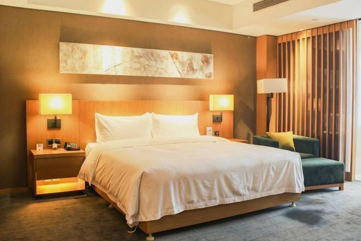 A hotel room with a large bed, two bedside tables with lamps, a green armchair, and a large abstract painting on the wall.