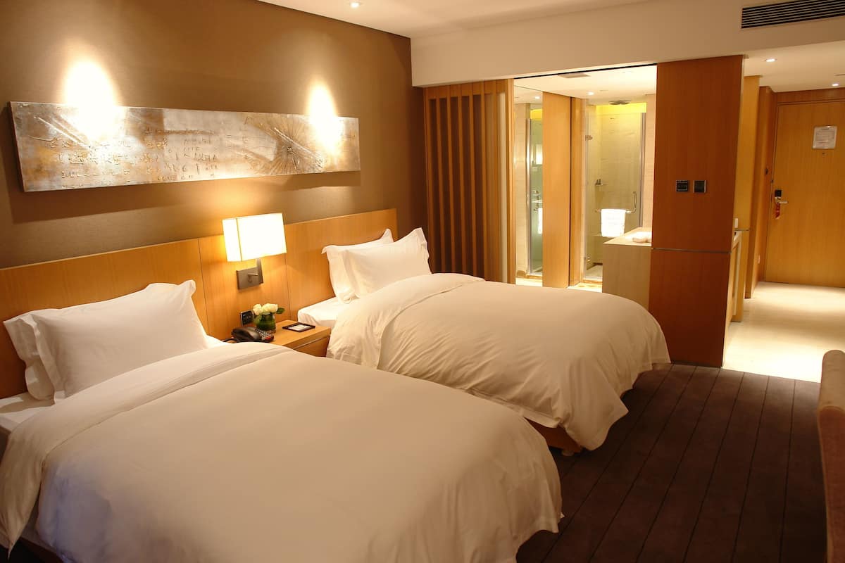 A hotel room with two beds, a nightstand with a lamp, and a large abstract painting on the wall.