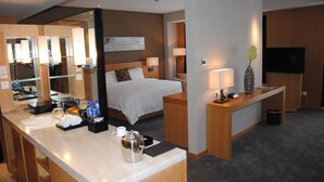A hotel room with a bed, bedside table, lamp, TV, and a bathroom with a mirror, sink, and towel rack. - Tian Feng International Hotel (Shenyang)