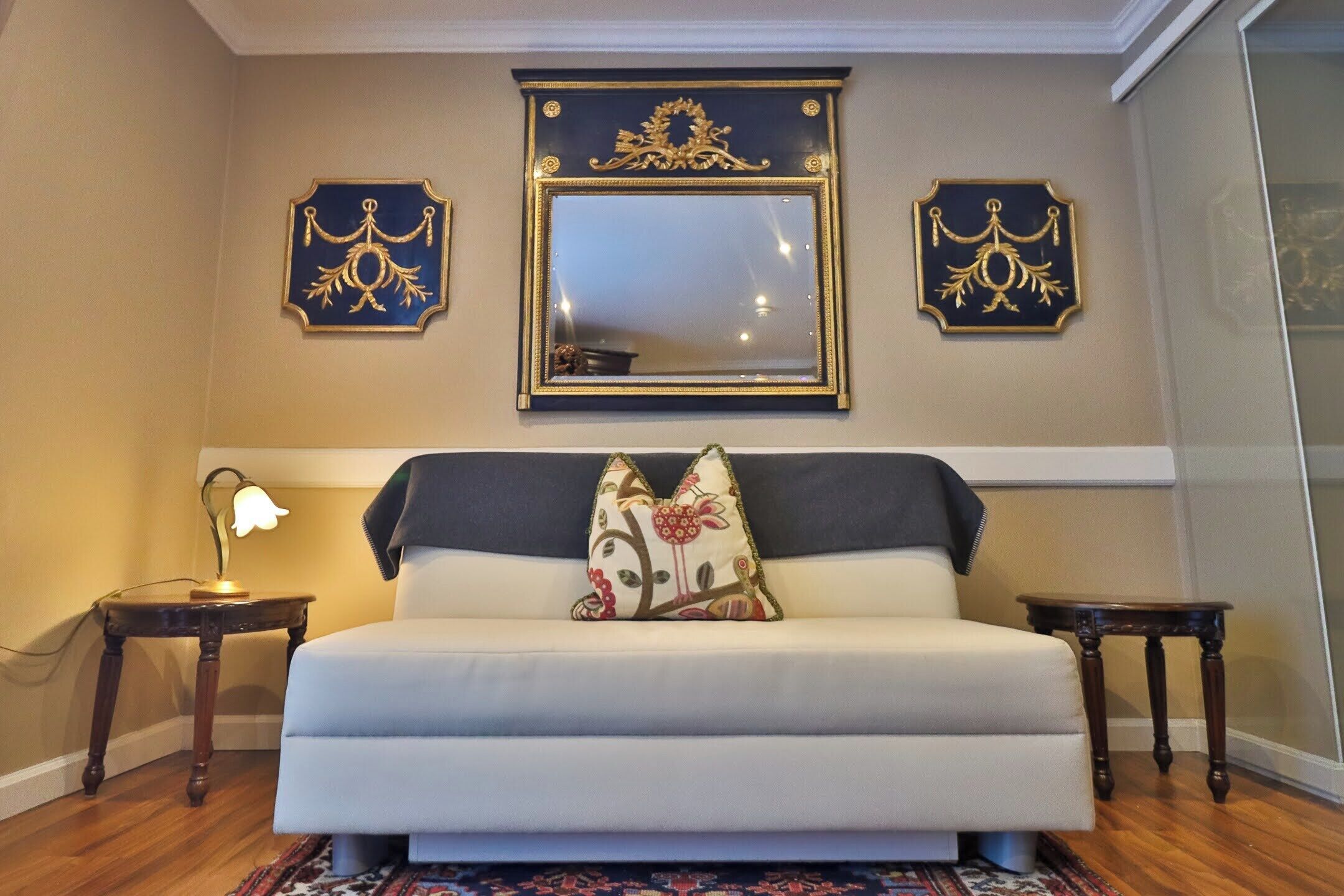 A bedroom with a bed, two nightstands, a lamp, and decorative wall mirrors.