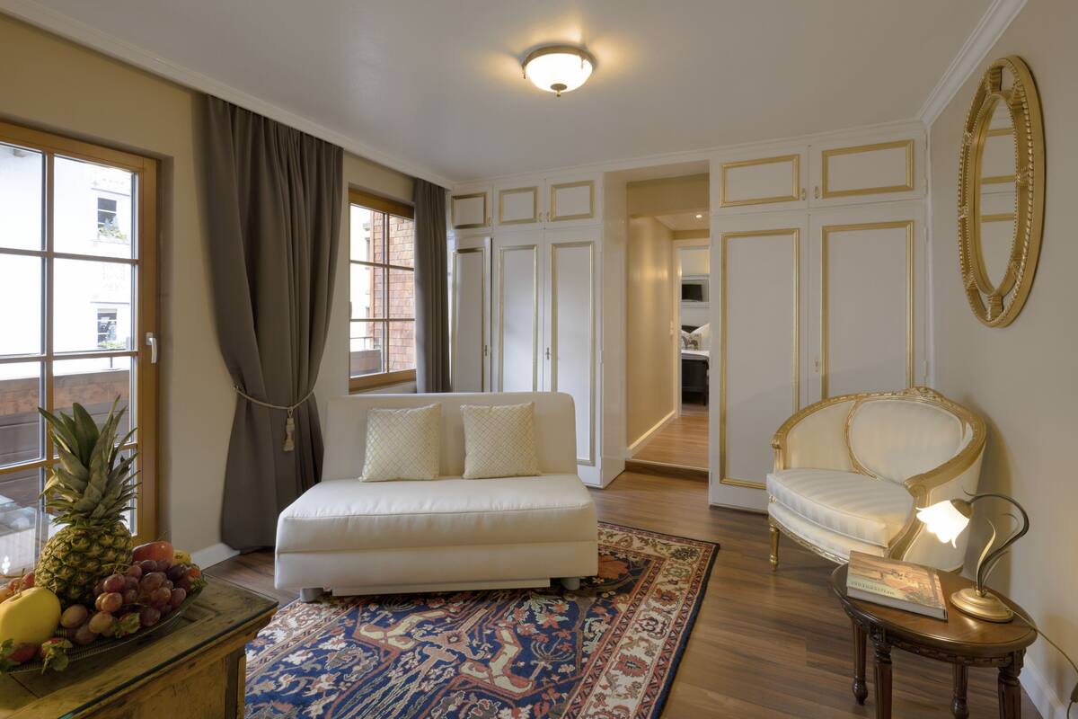 A bedroom with a bed, a chair, a table with a lamp, and a fruit bowl.