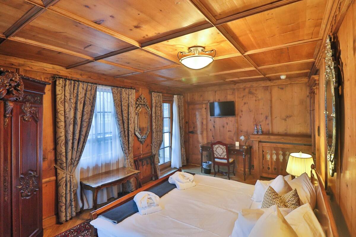 A wooden room with a bed, a desk, a chair, a television, and a lamp.