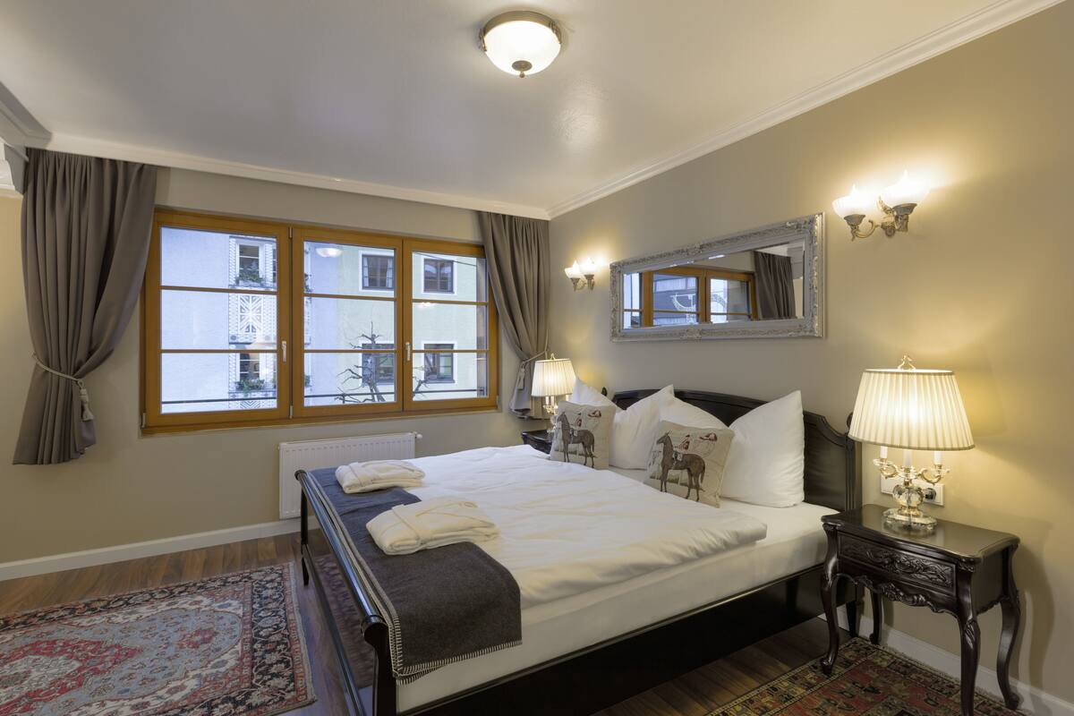 A hotel room with a large bed, two bedside lamps, a mirror, and a view of the outside through a window.