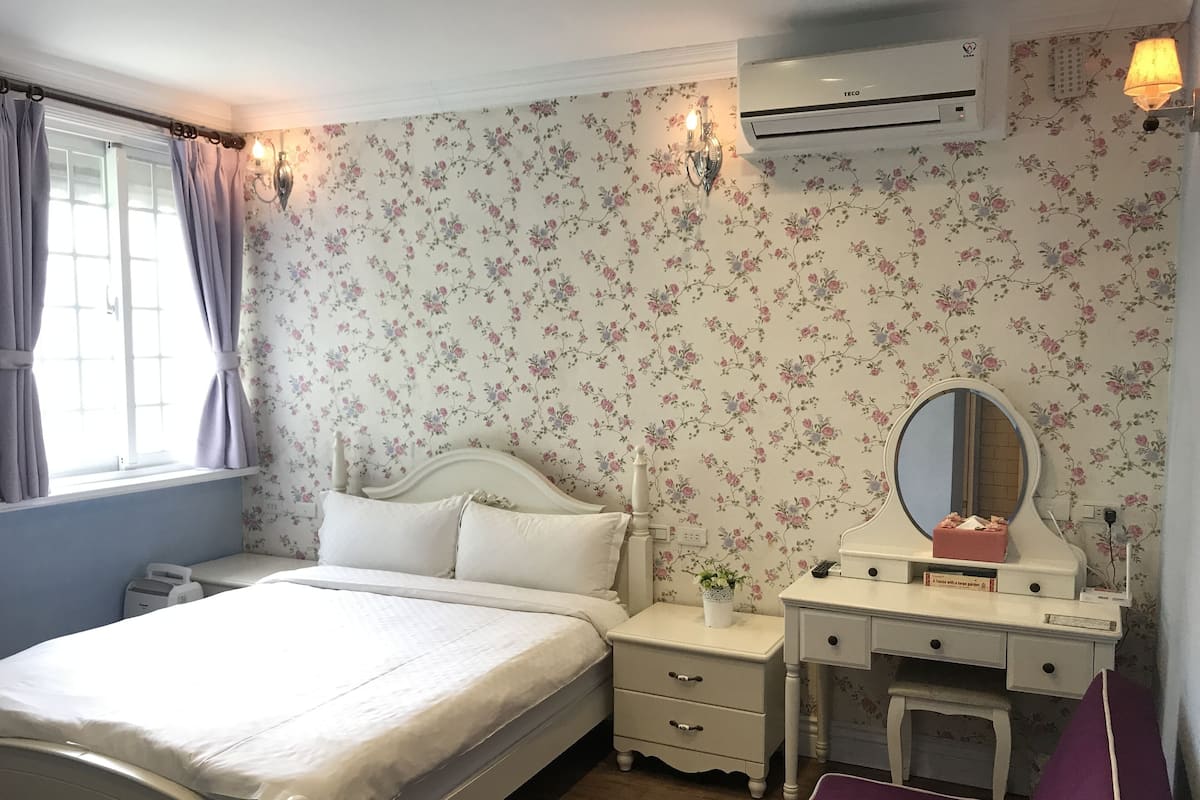 A bedroom with a bed, a nightstand, a dresser, a mirror, and an air conditioning unit.