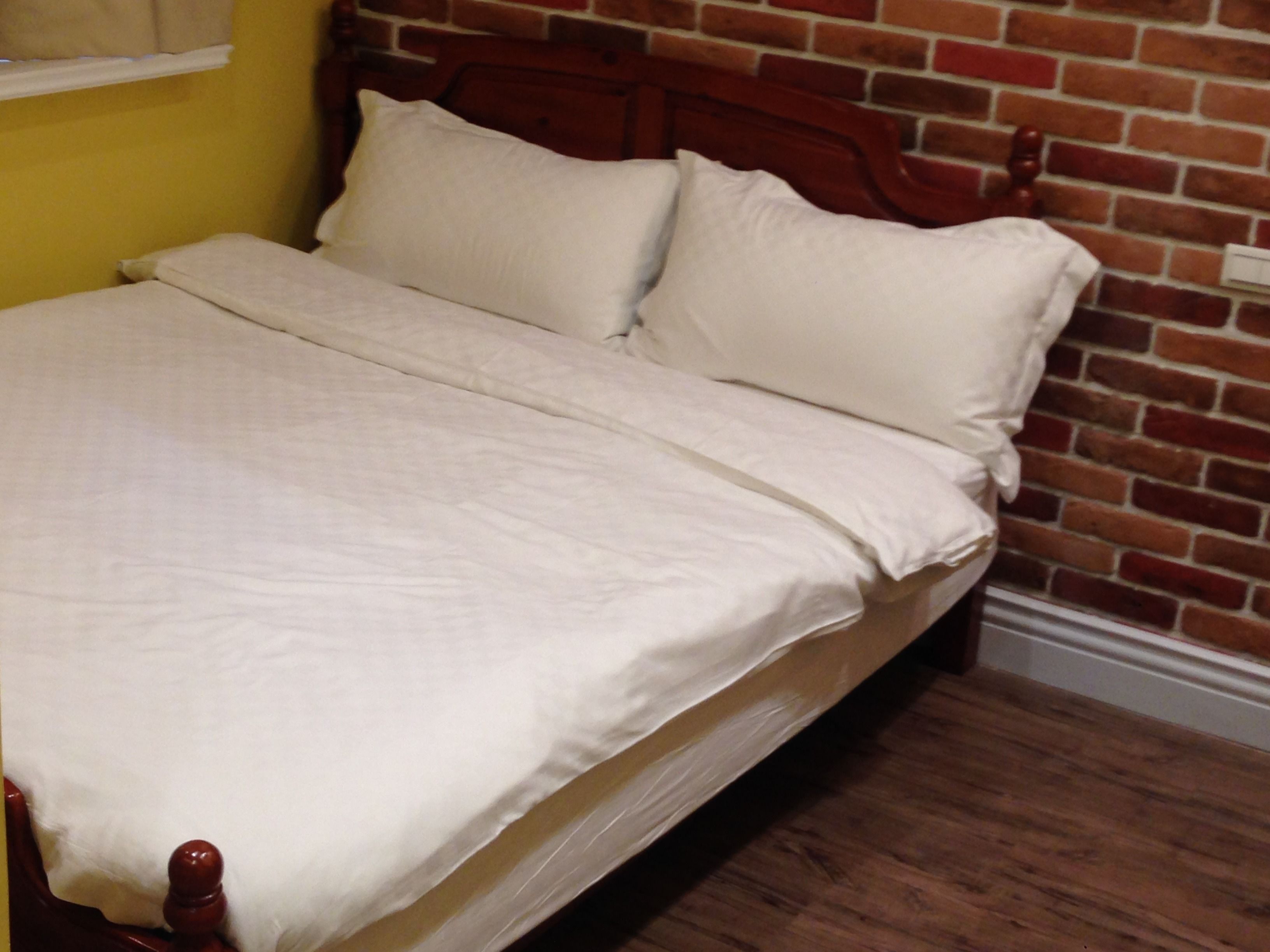 A bed with white bedding in a room with a brick wall and wooden floor.