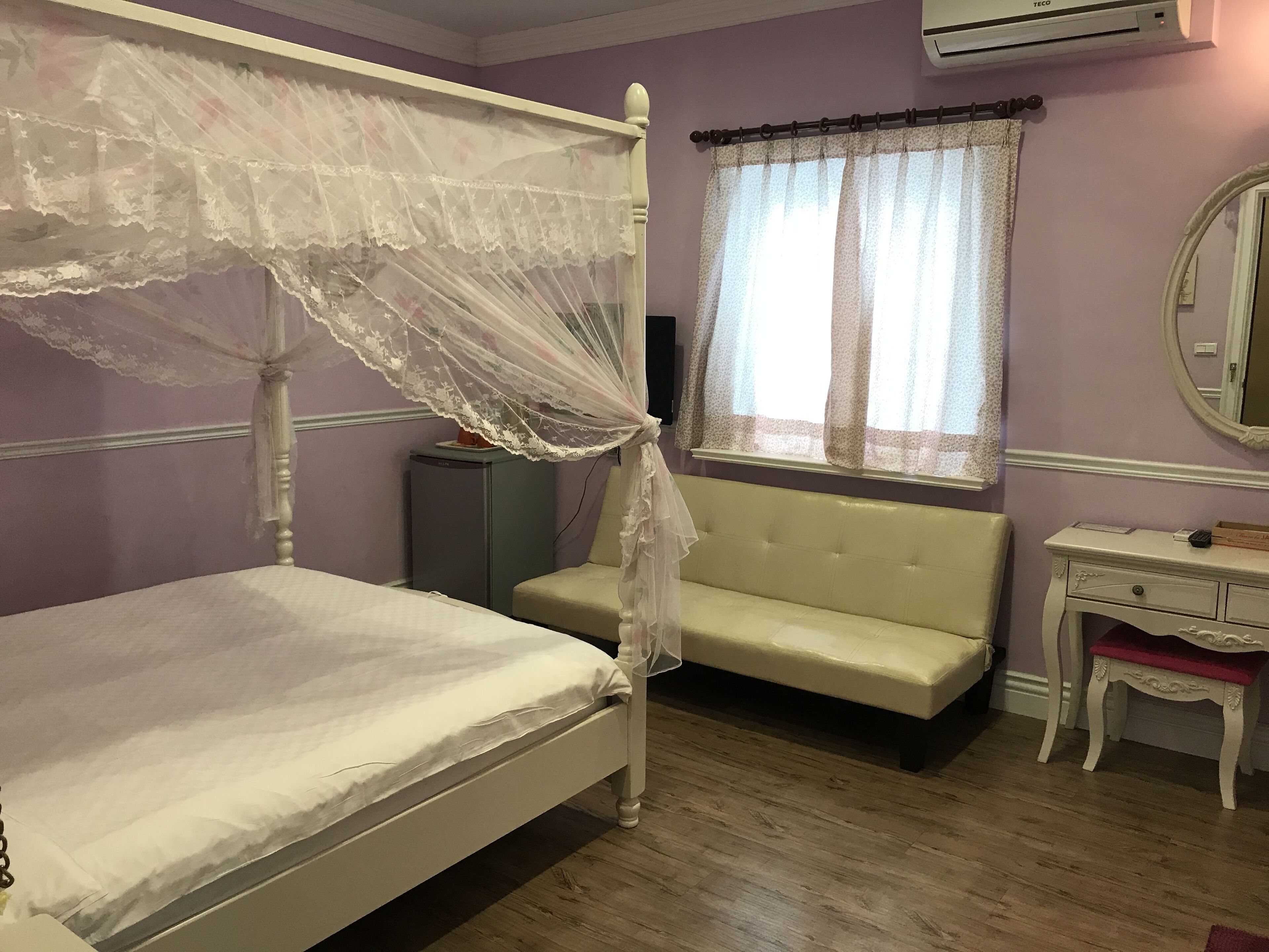 A bedroom with a four-poster bed, a bedside table, a small cabinet, and a window with curtains.