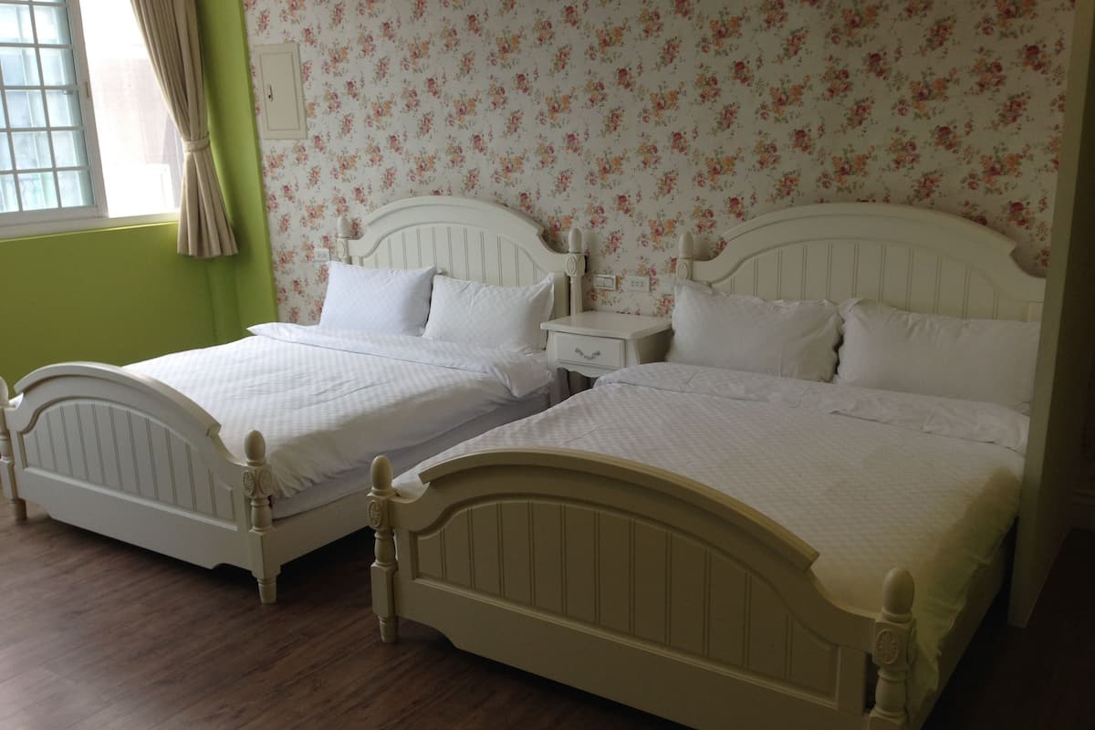 A room with two white beds, a nightstand, and a window with curtains.